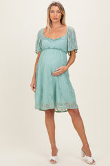 woman wearing a light mint green lace maternity dress with short puff sleeves and a visible baby bump