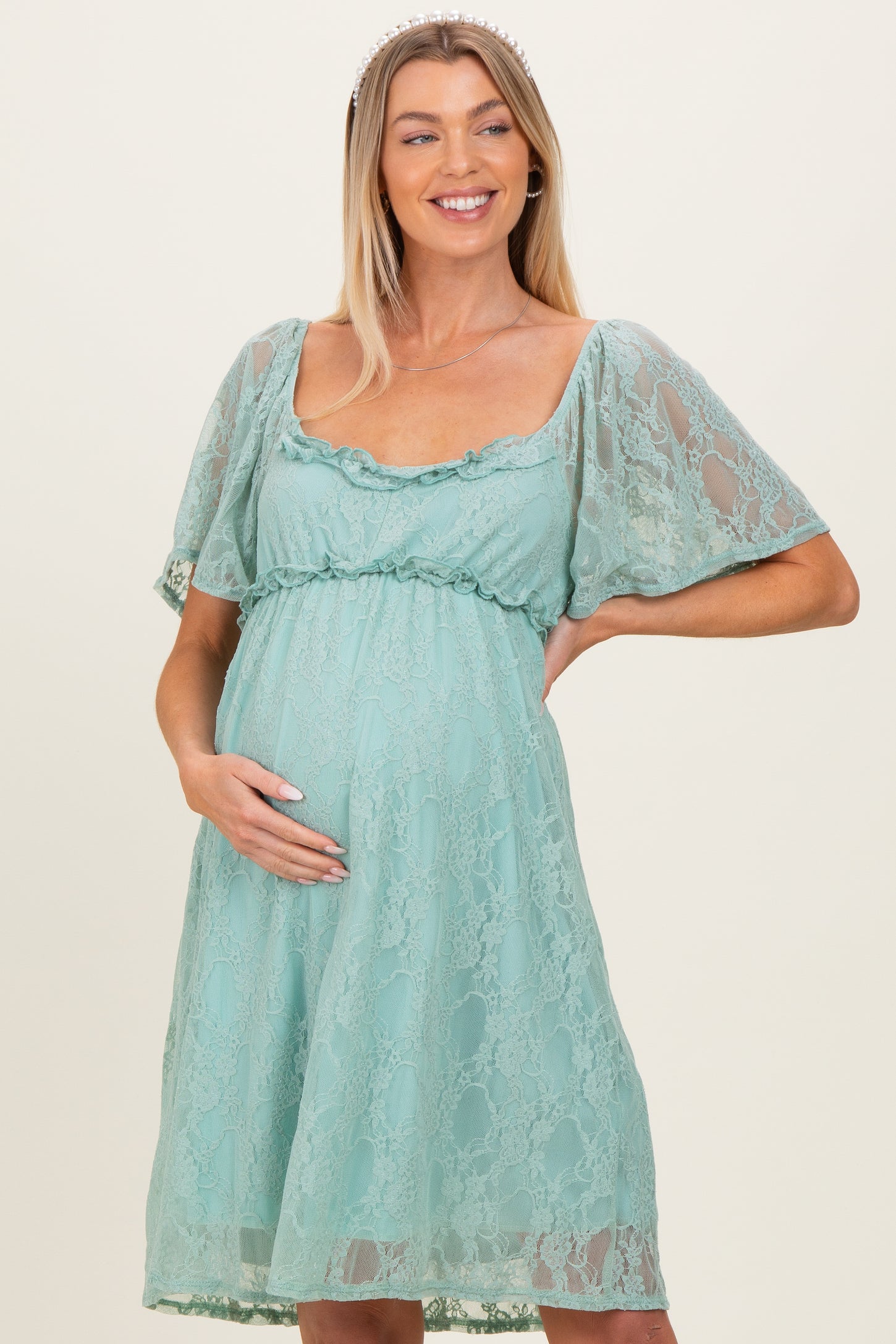 woman wearing a teal lace maternity dress with flutter sleeves and holding her baby bump