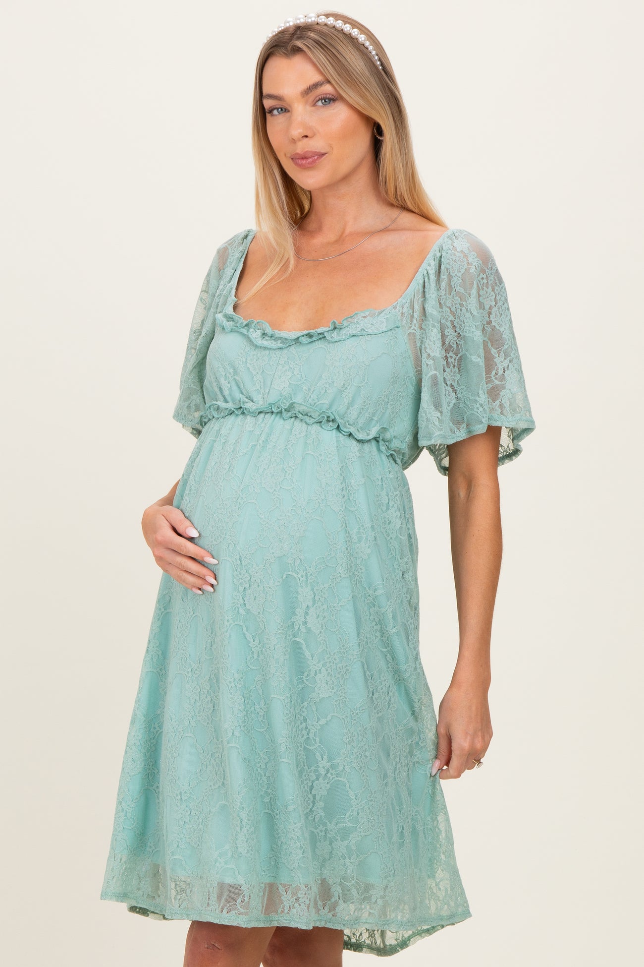 woman wearing a mint green lace maternity dress with short sleeves and holding her baby bump