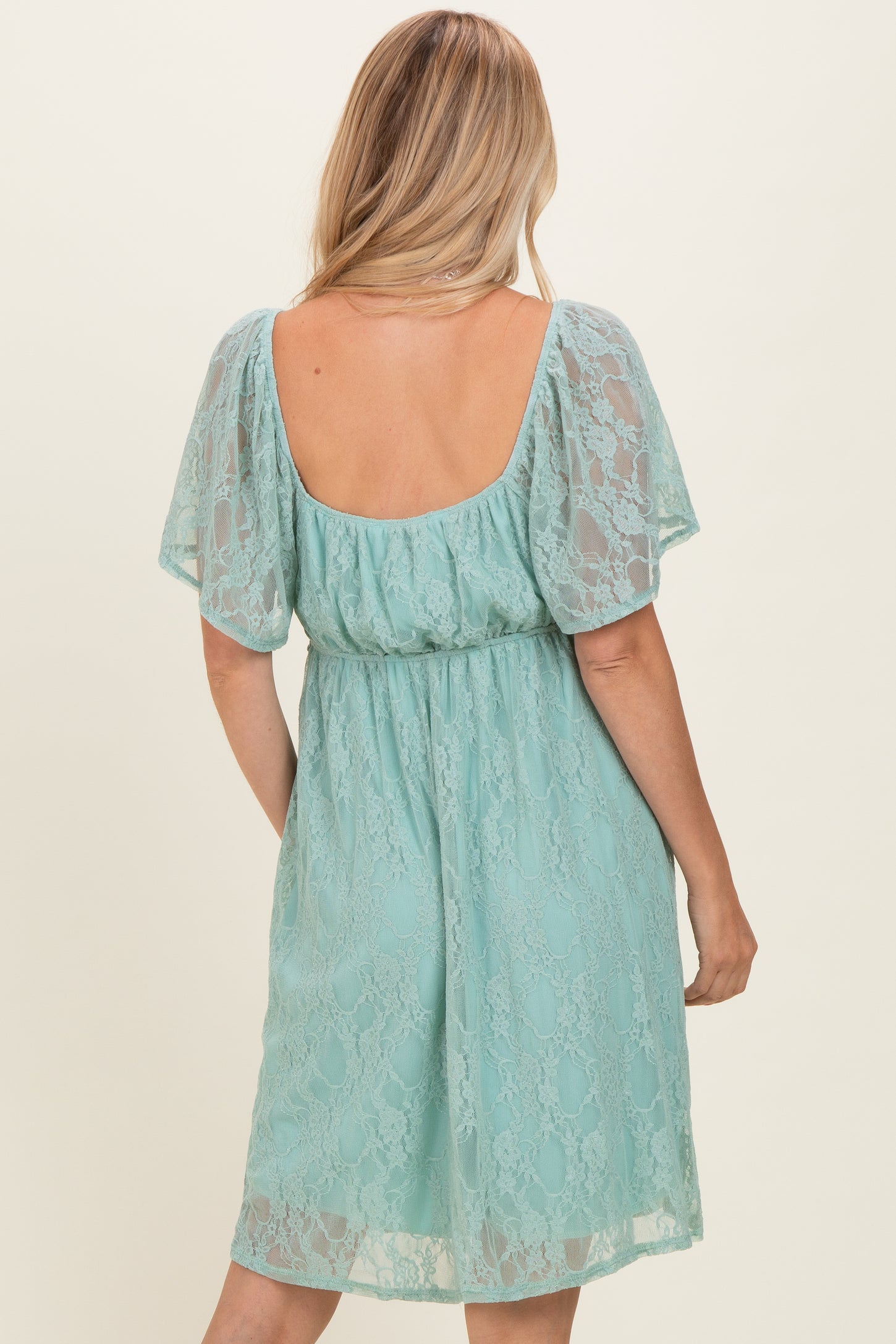woman wearing a backless light teal lace dress with short sleeves and a fitted waist