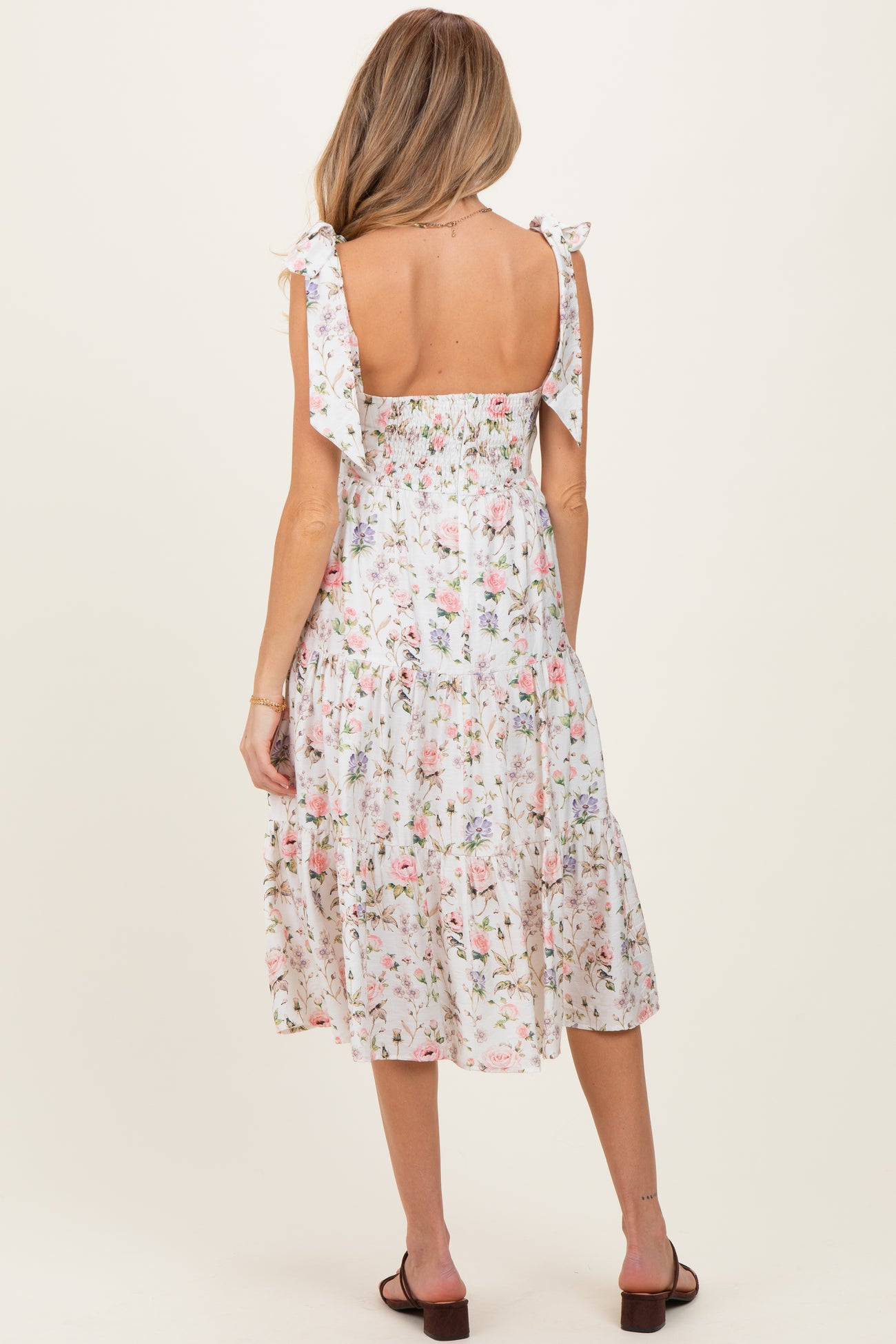 woman wearing a floral print maternity dress with ruffled straps and a tiered skirt, showing her back and a baby bump