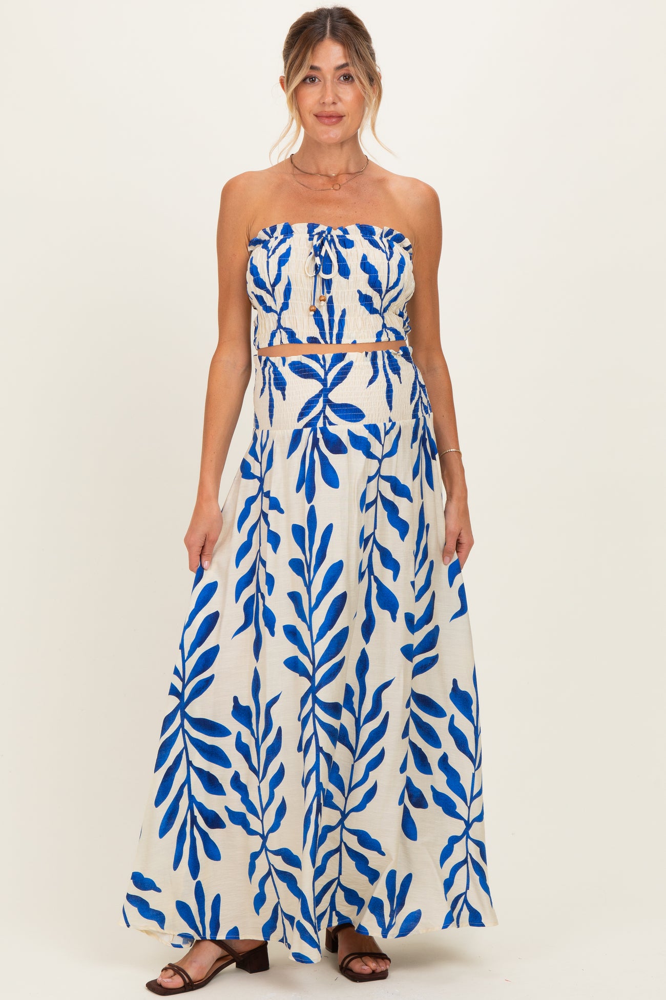 woman wearing a maternity two-piece set with a strapless crop top and a long skirt featuring a blue leaf print