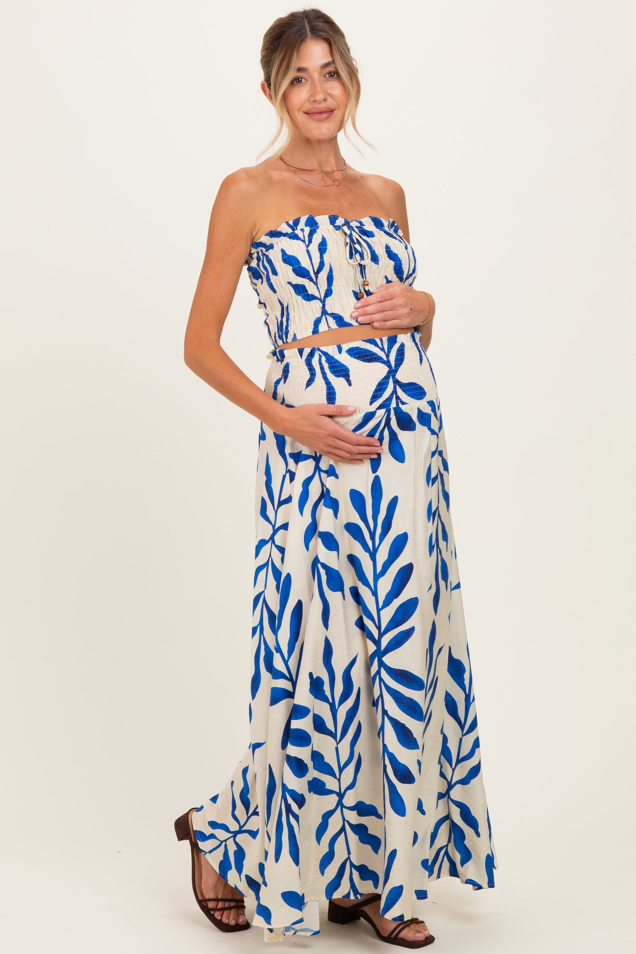 woman wearing a strapless blue and white floral print maternity dress and gently cradling her baby bump