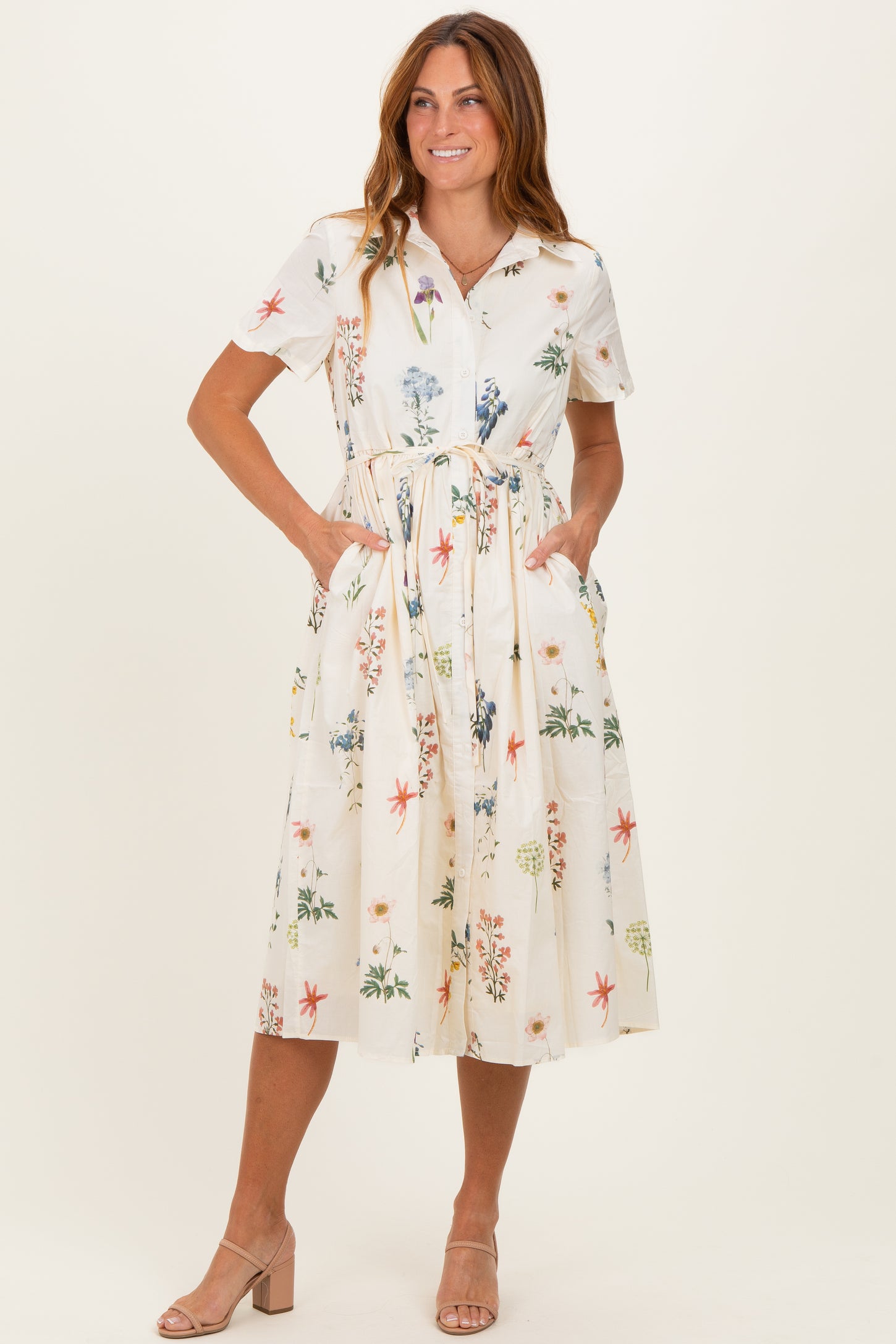 woman wearing a short sleeve floral midi dress with a belted waist and pockets, styled with beige heels