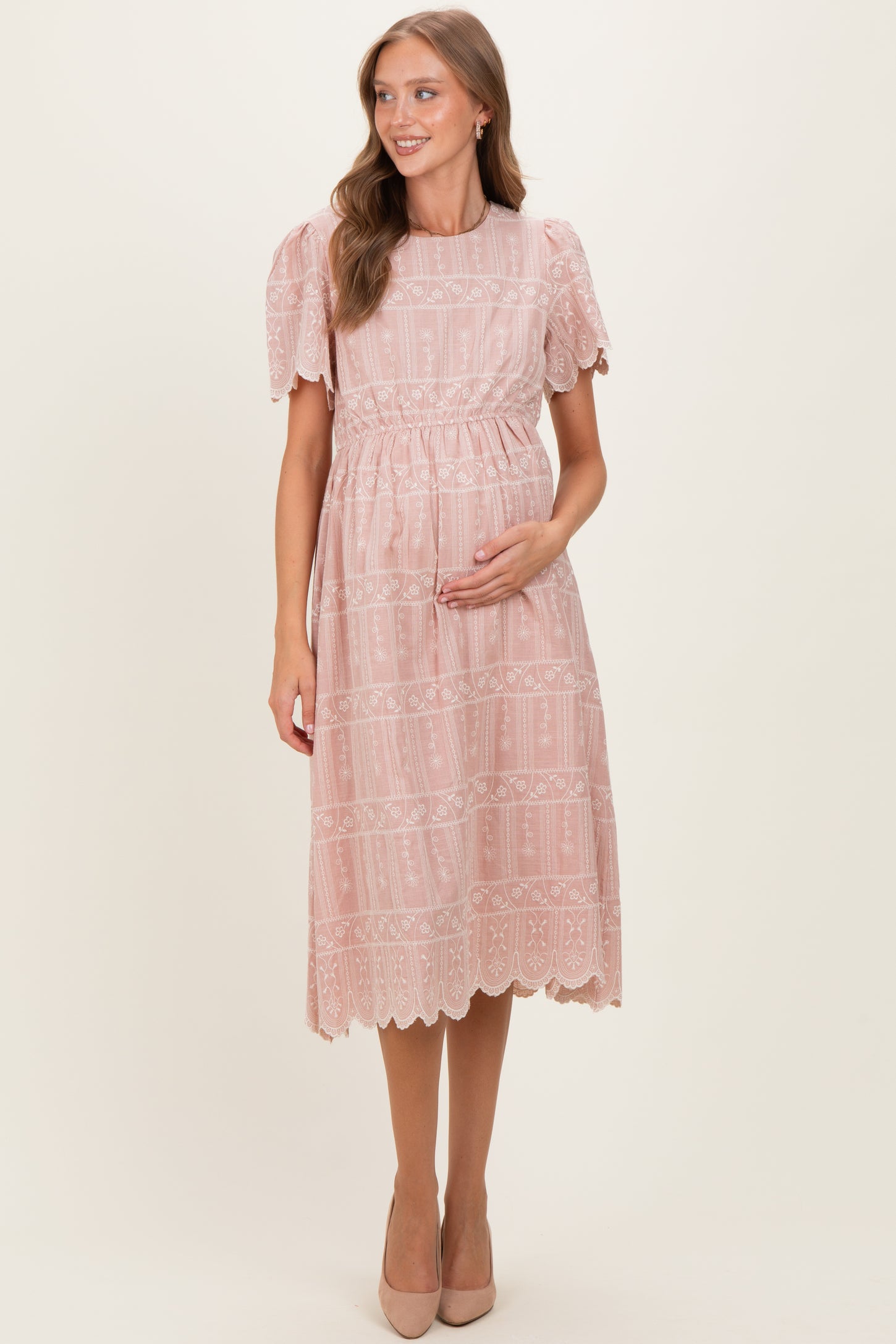 woman wearing a dusty pink lace maternity dress with short puff sleeves and a baby bump