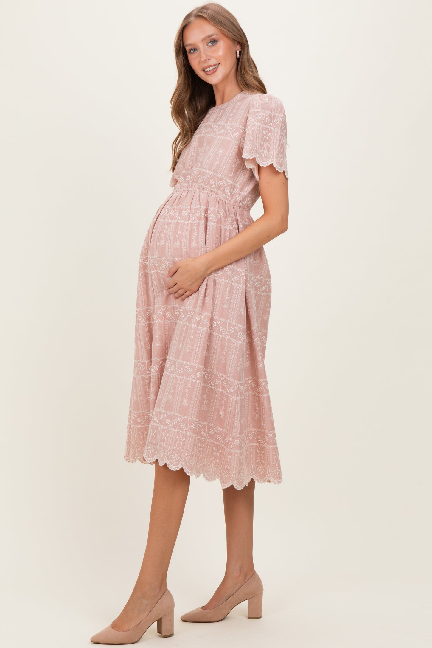woman wearing a pink lace trim maternity dress with a tiered design and holding her baby bump