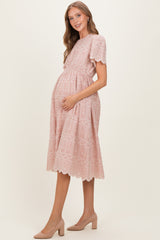 woman wearing a pink lace trim maternity dress with a tiered design and holding her baby bump