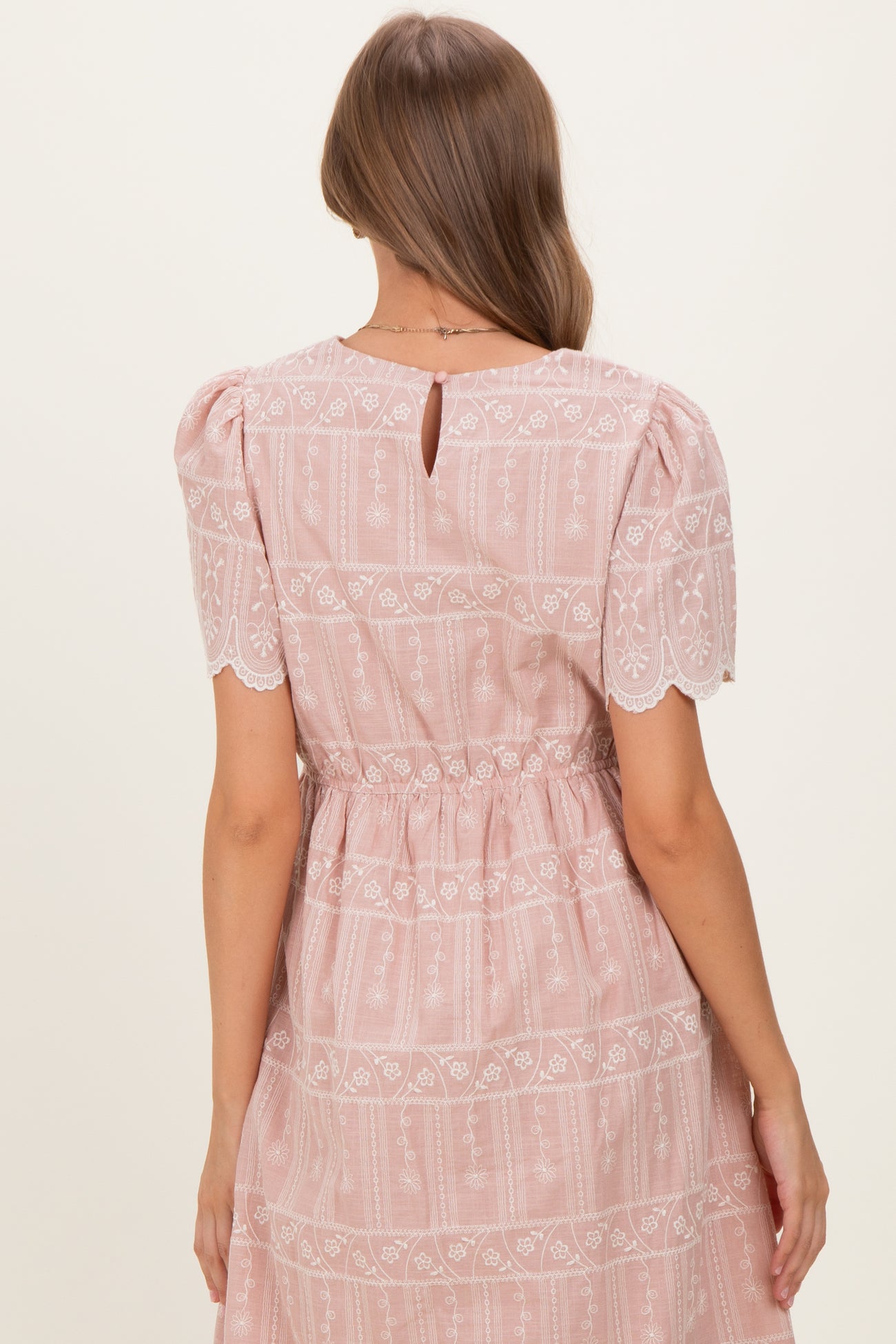 woman wearing a pink maternity dress with puff sleeves and lace detailing, showing the back view