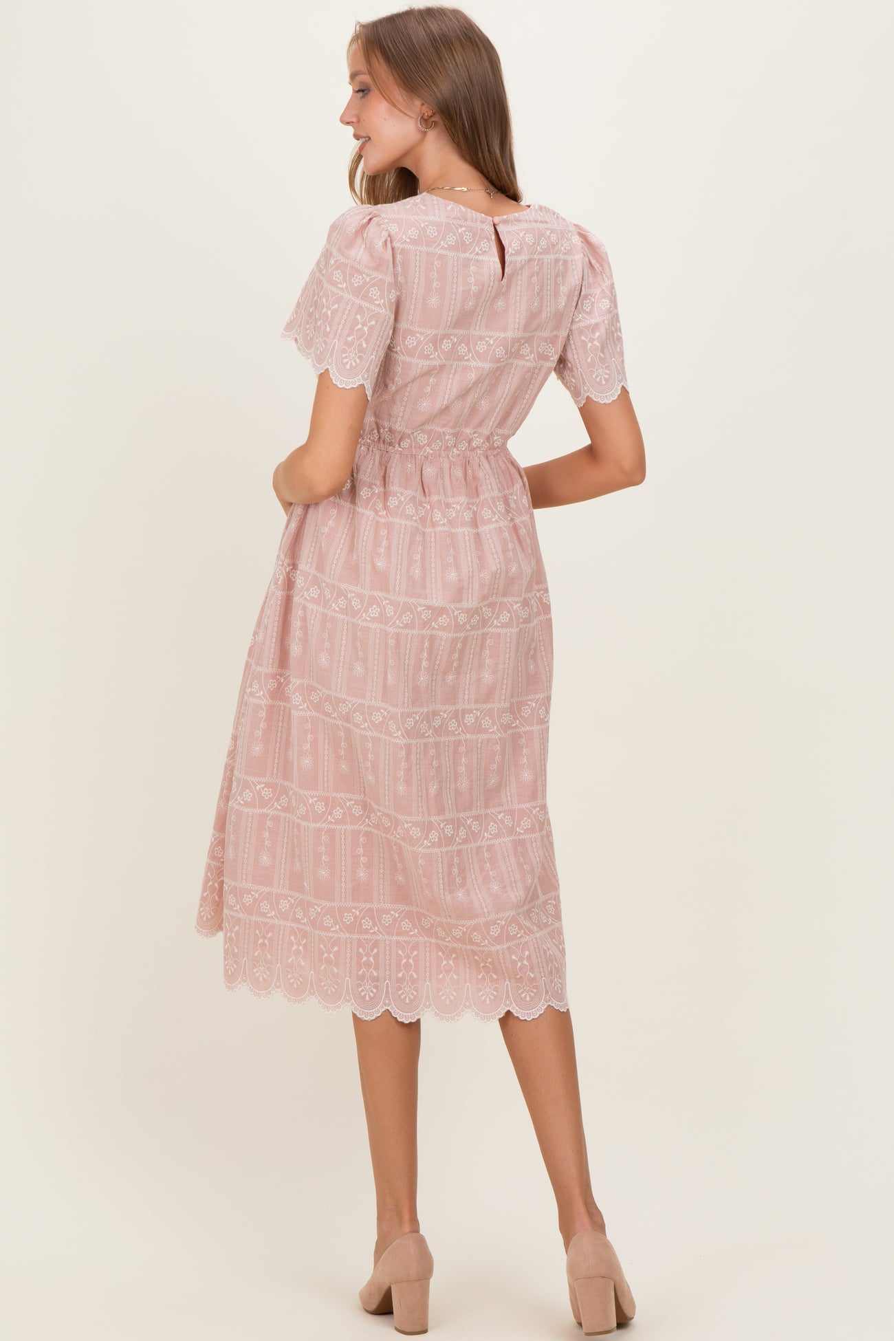 woman wearing a light pink maternity dress with lace details and short sleeves, styled with a cinched waist and flowing skirt