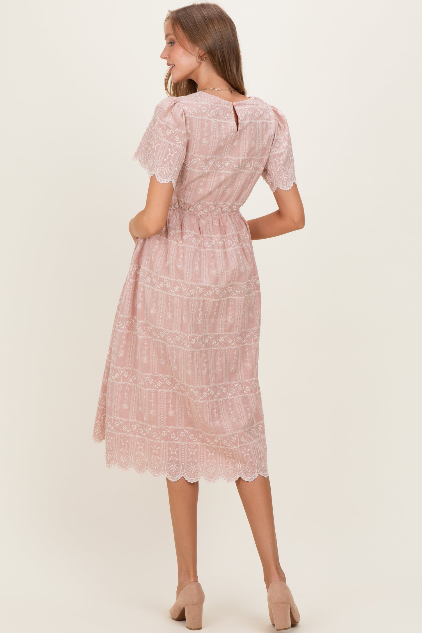 woman wearing a light pink maternity dress with lace details and short sleeves, styled with a cinched waist and flowing skirt