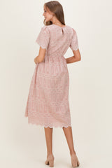 woman wearing a light pink maternity dress with lace details and short sleeves, styled with a cinched waist and flowing skirt