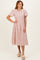 woman wearing a light pink embroidered midi dress with short ruffled sleeves and a fitted waist, standing on a neutral background