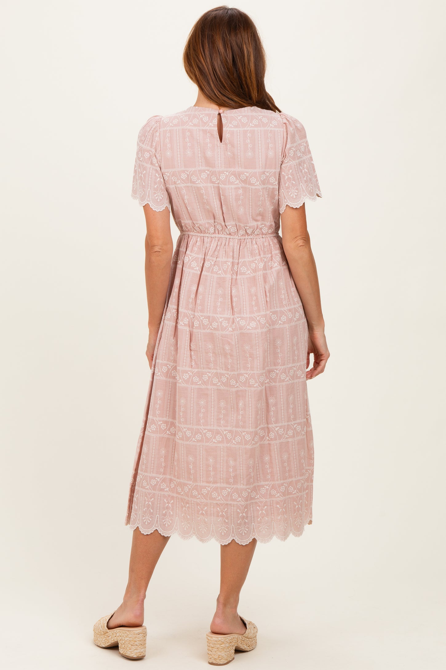 woman wearing a blush pink midi dress with lace details and a cinched waist, shown from the back