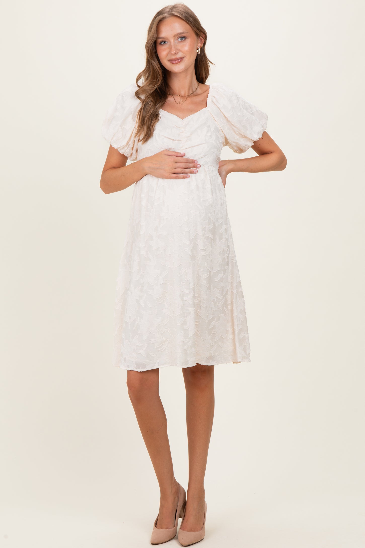 woman wearing a white maternity dress with puff sleeves and textured pattern, holding her baby bump