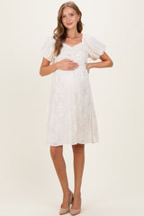woman wearing a white maternity dress with puff sleeves and textured pattern, holding her baby bump