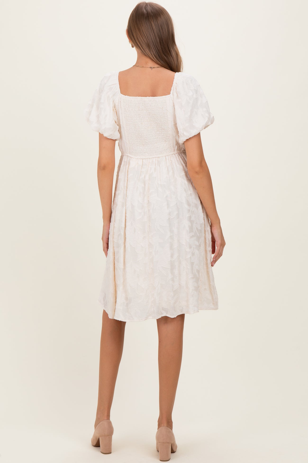 woman wearing a white floral maternity dress with puff sleeves and a fitted waist, showing her baby bump from the back