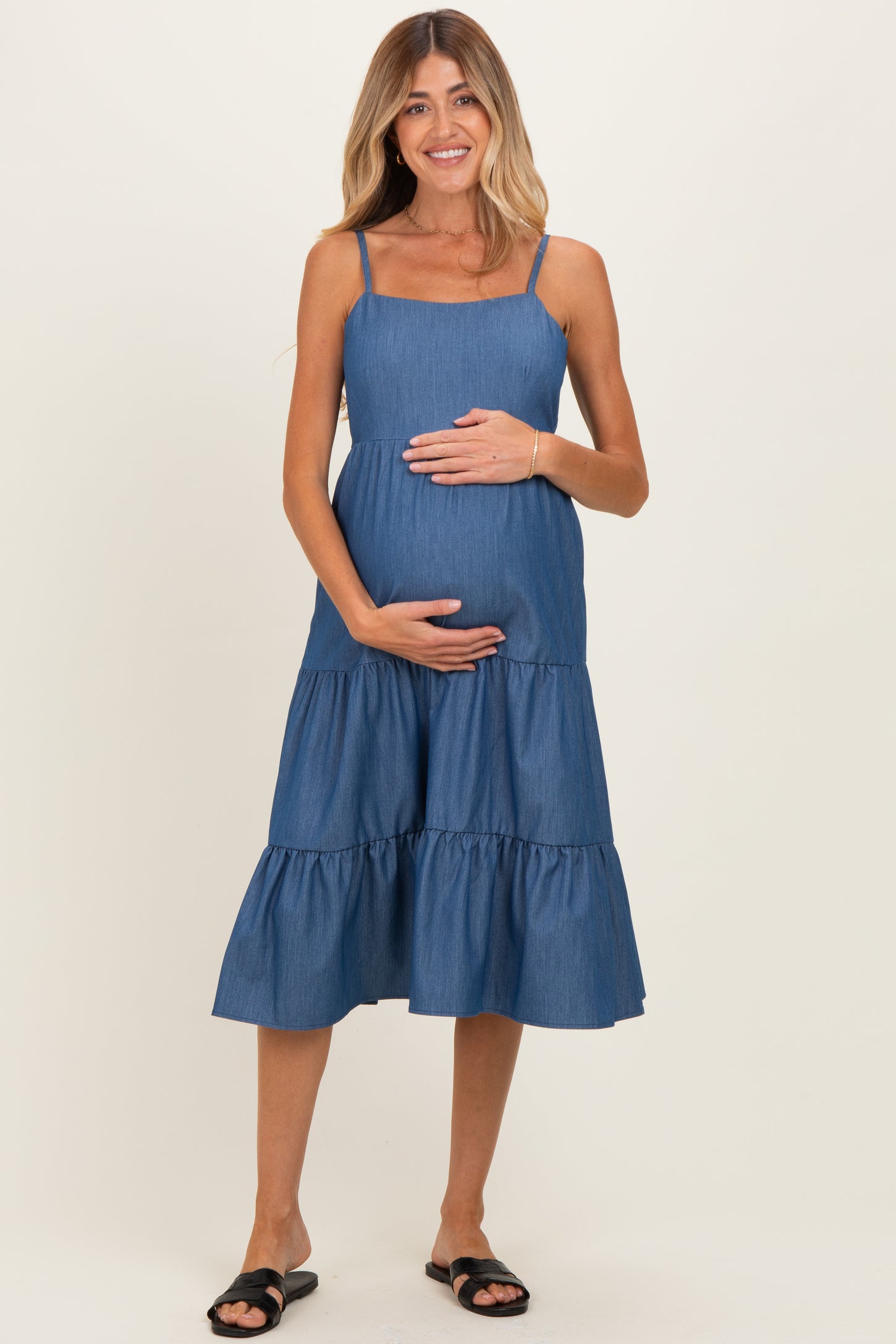 woman wearing a blue tiered maternity dress and cradling her baby bump