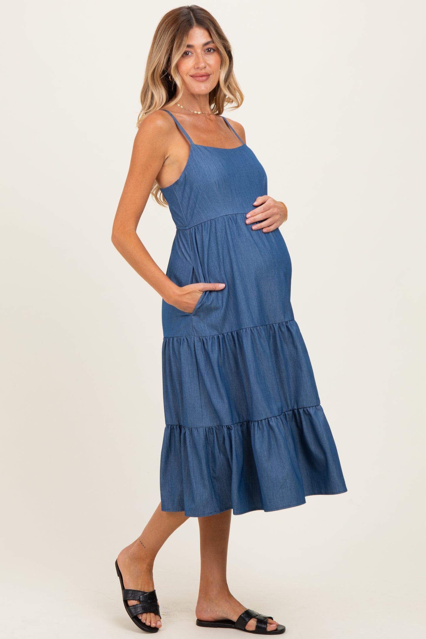 woman wearing a blue tiered maternity dress with pockets and holding her baby bump