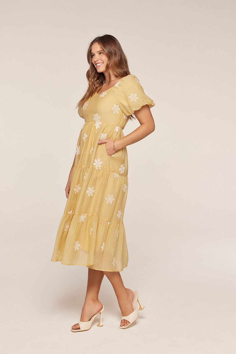 woman wearing a yellow floral embroidered midi dress with puff sleeves and pockets