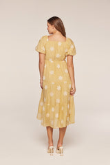 woman wearing a yellow tiered midi dress with floral embroidery and puff sleeves, shown from the back