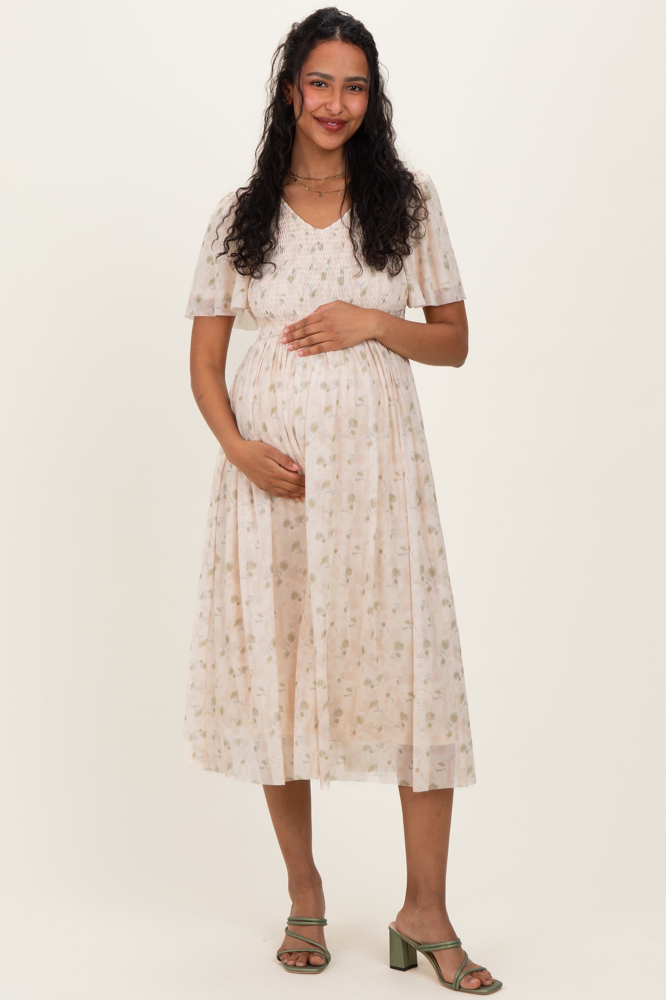 woman wearing a cream floral maternity dress with short sleeves and a gathered waist, holding her baby bump