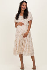 woman wearing a light pink floral maternity dress with a v-neck and short sleeves, gently holding her baby bump