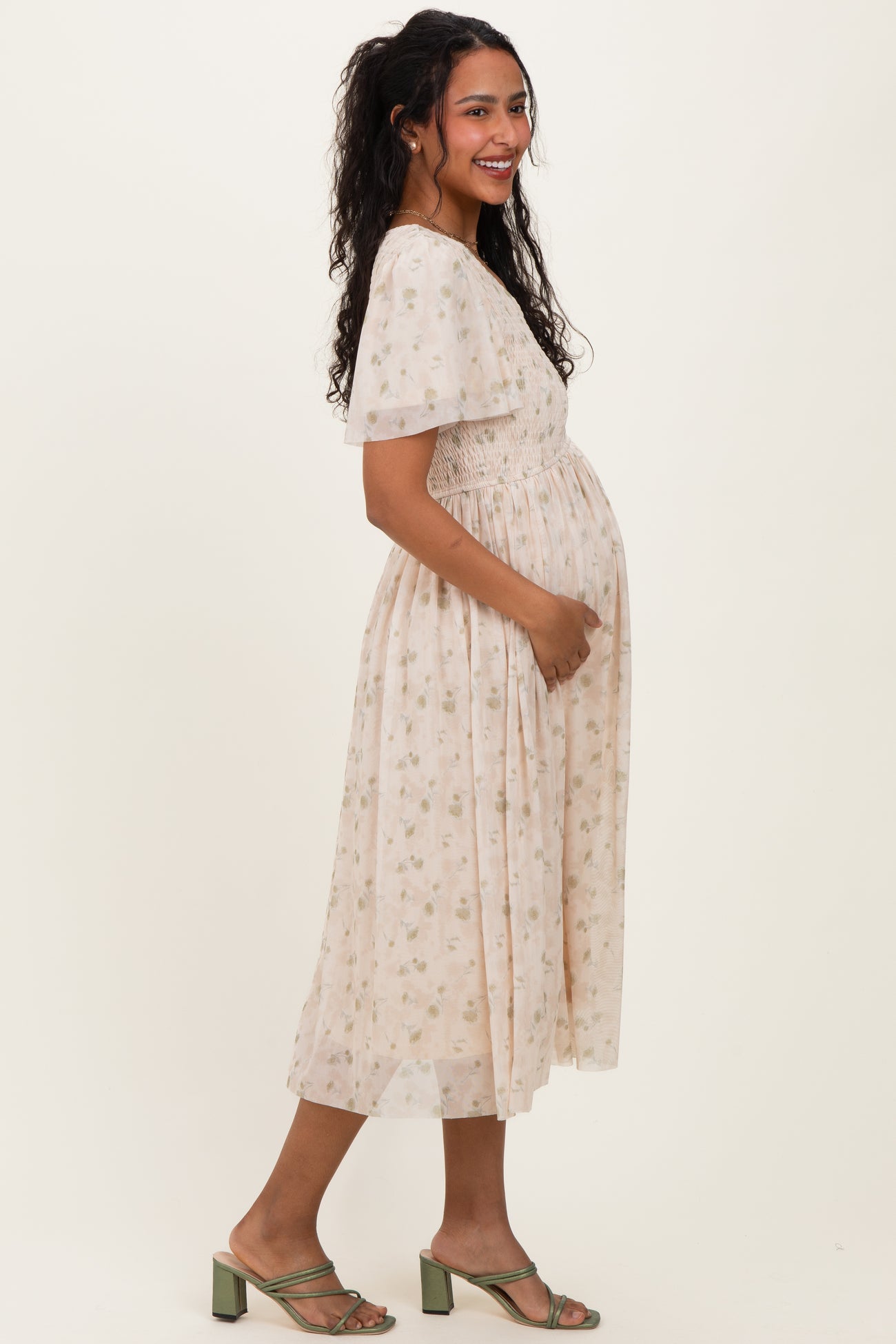 woman wearing a floral maternity dress with a smocked bodice and short flutter sleeves, cradling her baby bump