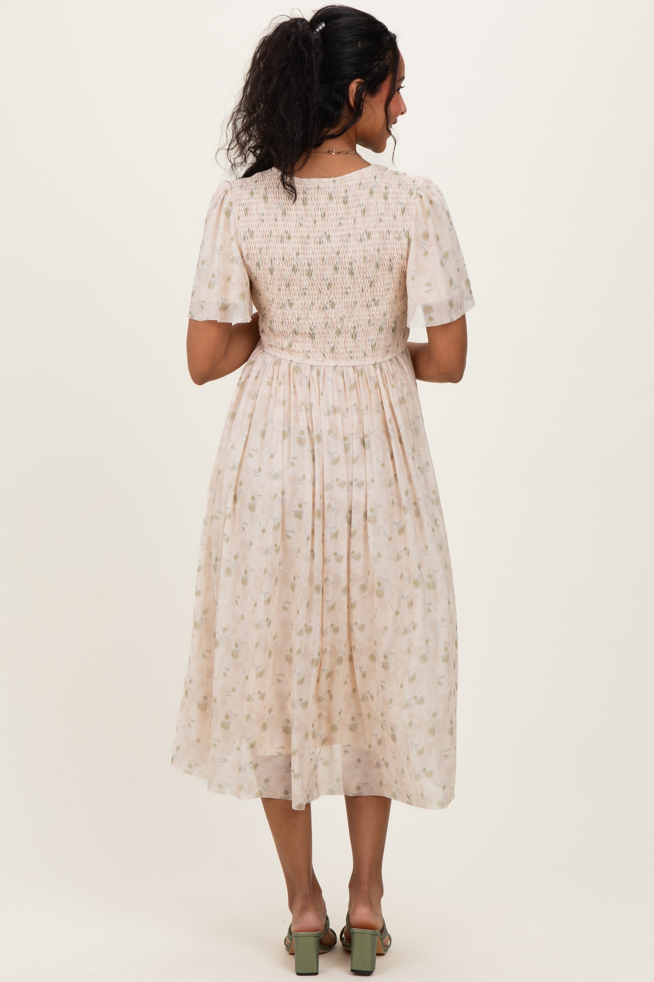 woman wearing a short sleeve light pink maternity dress with a floral pattern and smocked bodice, showing her baby bump