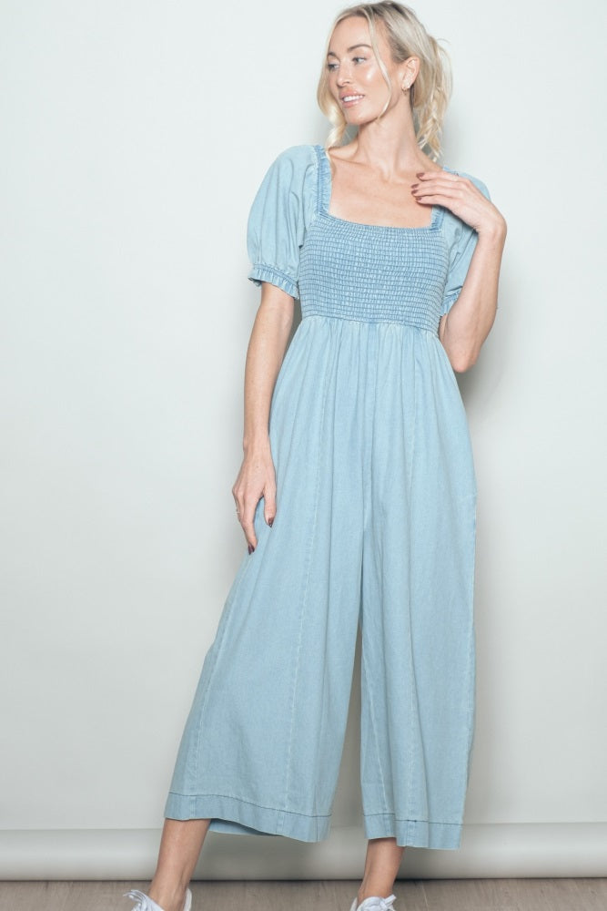 woman wearing a light blue puff sleeve jumpsuit with a smocked bodice and wide-leg pants