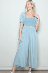 woman wearing a light blue puff sleeve jumpsuit with a smocked bodice and wide-leg pants