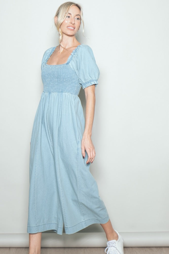 woman wearing a light blue smocked waist midi dress with puff sleeves and side pockets