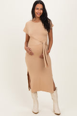 woman wearing a beige maternity dress with a tie waist and side slits, holding her baby bump
