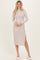 woman wearing a light beige ribbed long sleeve midi dress with a side slit and standing with a smile