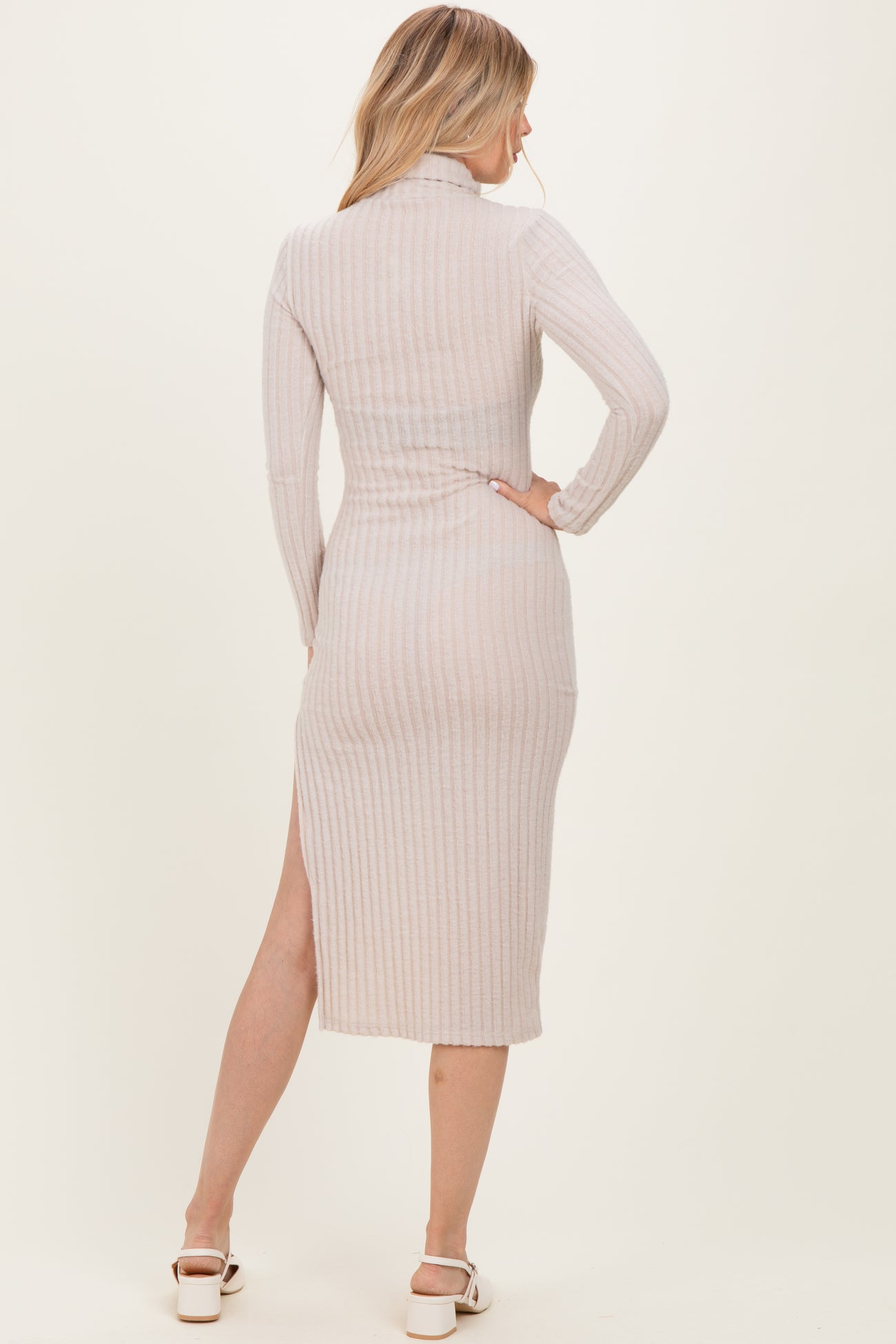 woman wearing a light beige ribbed midi dress with long sleeves and a side slit, viewed from the back