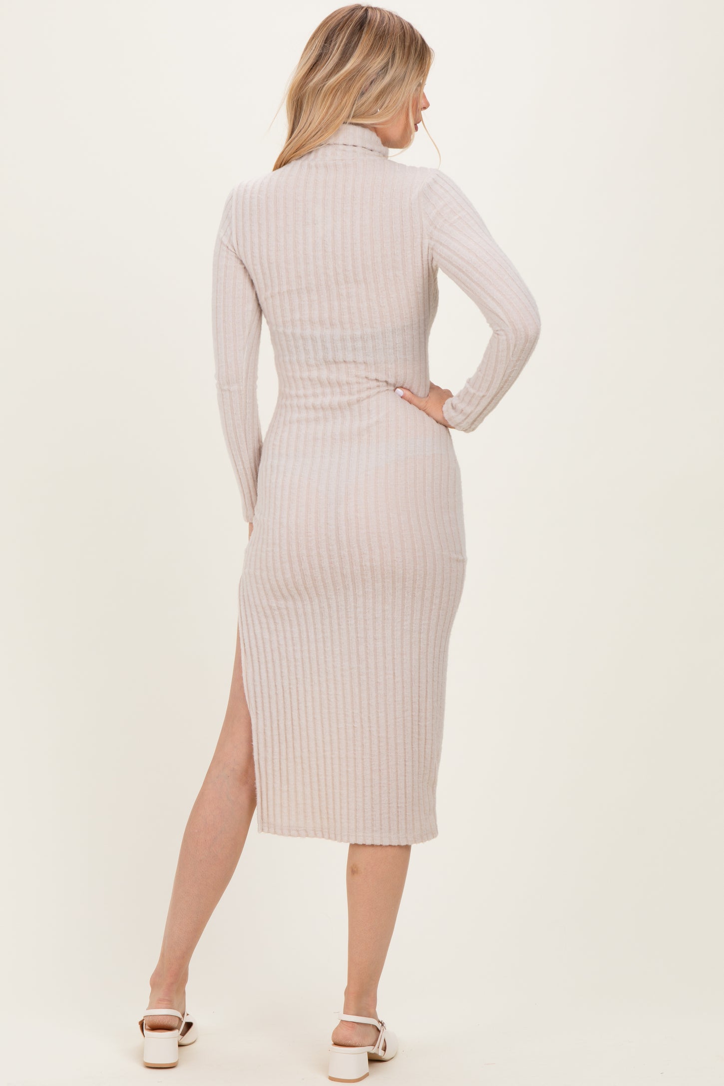 woman wearing a light beige ribbed midi dress with long sleeves and a side slit, viewed from the back
