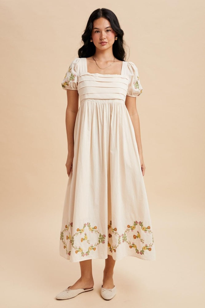 woman wearing a cream-colored midi dress with puff sleeves and floral embroidery at the hem