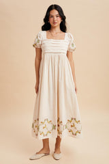 woman wearing a cream-colored midi dress with puff sleeves and floral embroidery at the hem