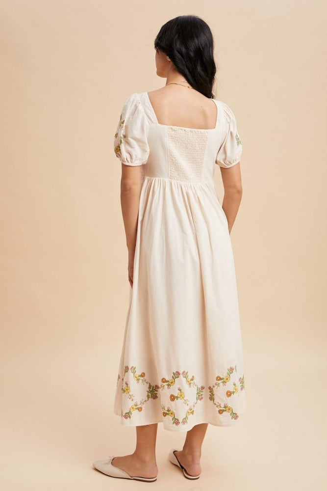 woman wearing a cream-colored midi dress with floral embroidery and puff sleeves, shown from the back