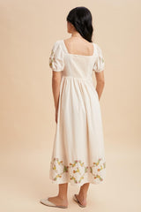 woman wearing a cream-colored midi dress with floral embroidery and puff sleeves, shown from the back