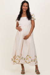 woman wearing a cream maternity dress with floral embroidery and puff sleeves, holding her baby bump