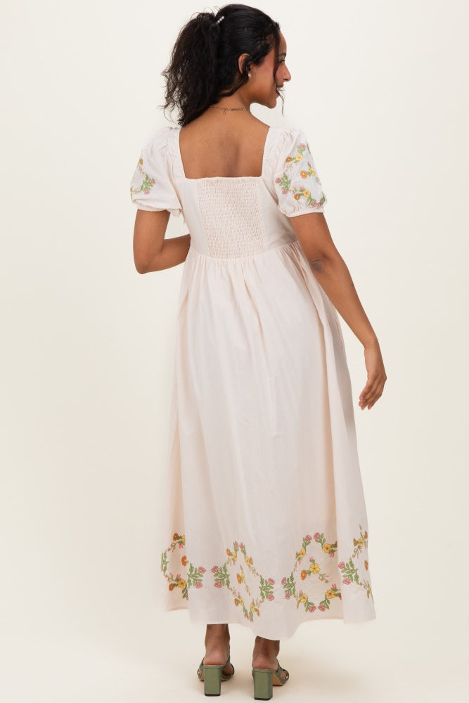 woman wearing a light pink maternity dress with floral embroidery on the hem and puff sleeves, showing a baby bump