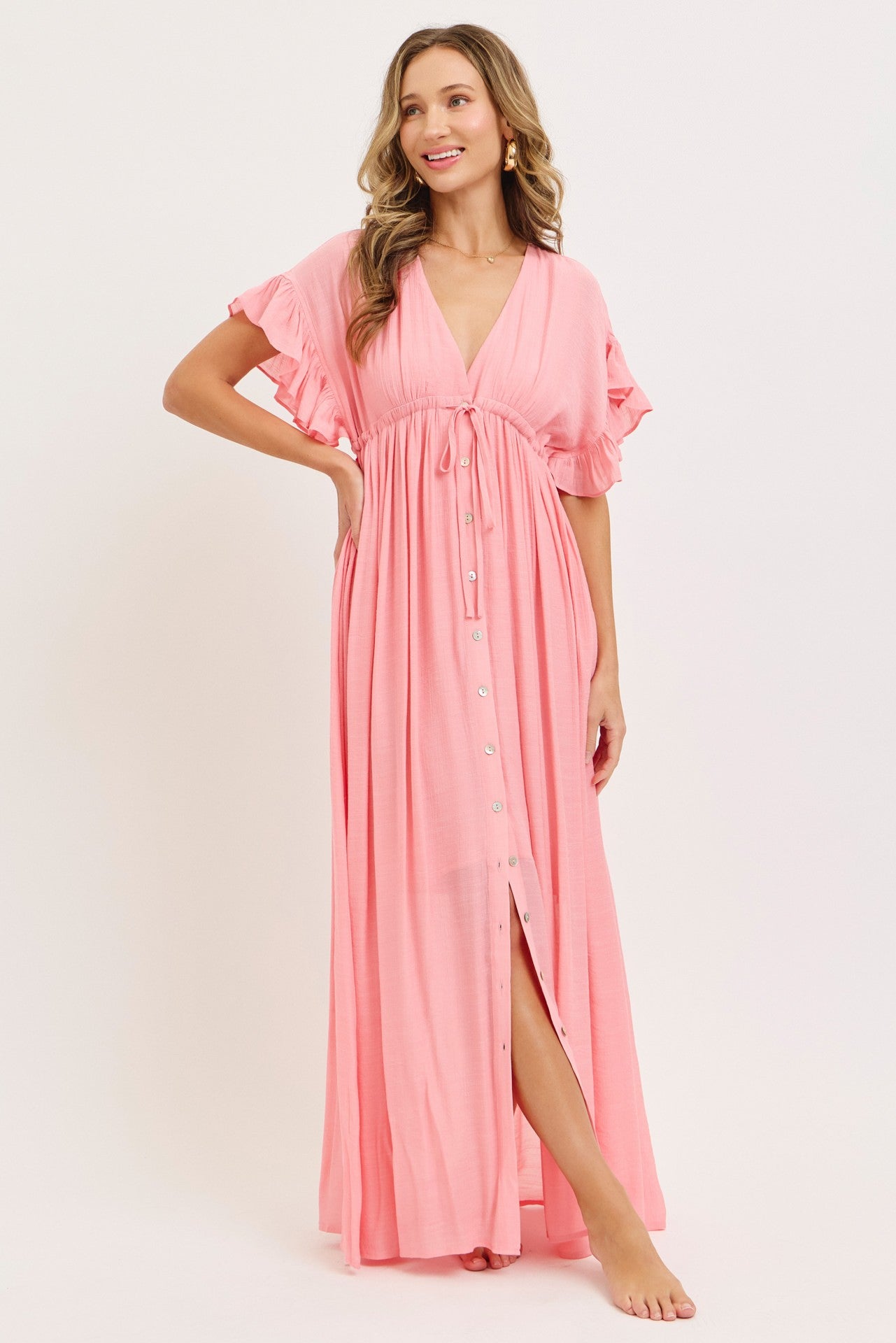 woman wearing a pink maxi dress with ruffle sleeves and a front slit, styled with a v-neckline and button details