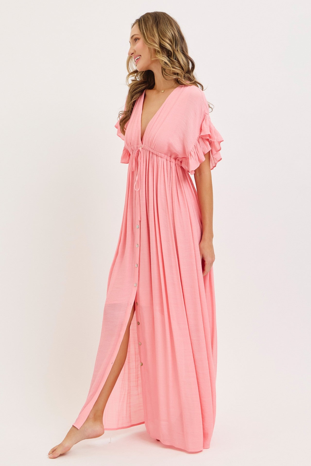 woman wearing a pink maxi dress with flutter sleeves and a cinched waist, featuring button details down the front