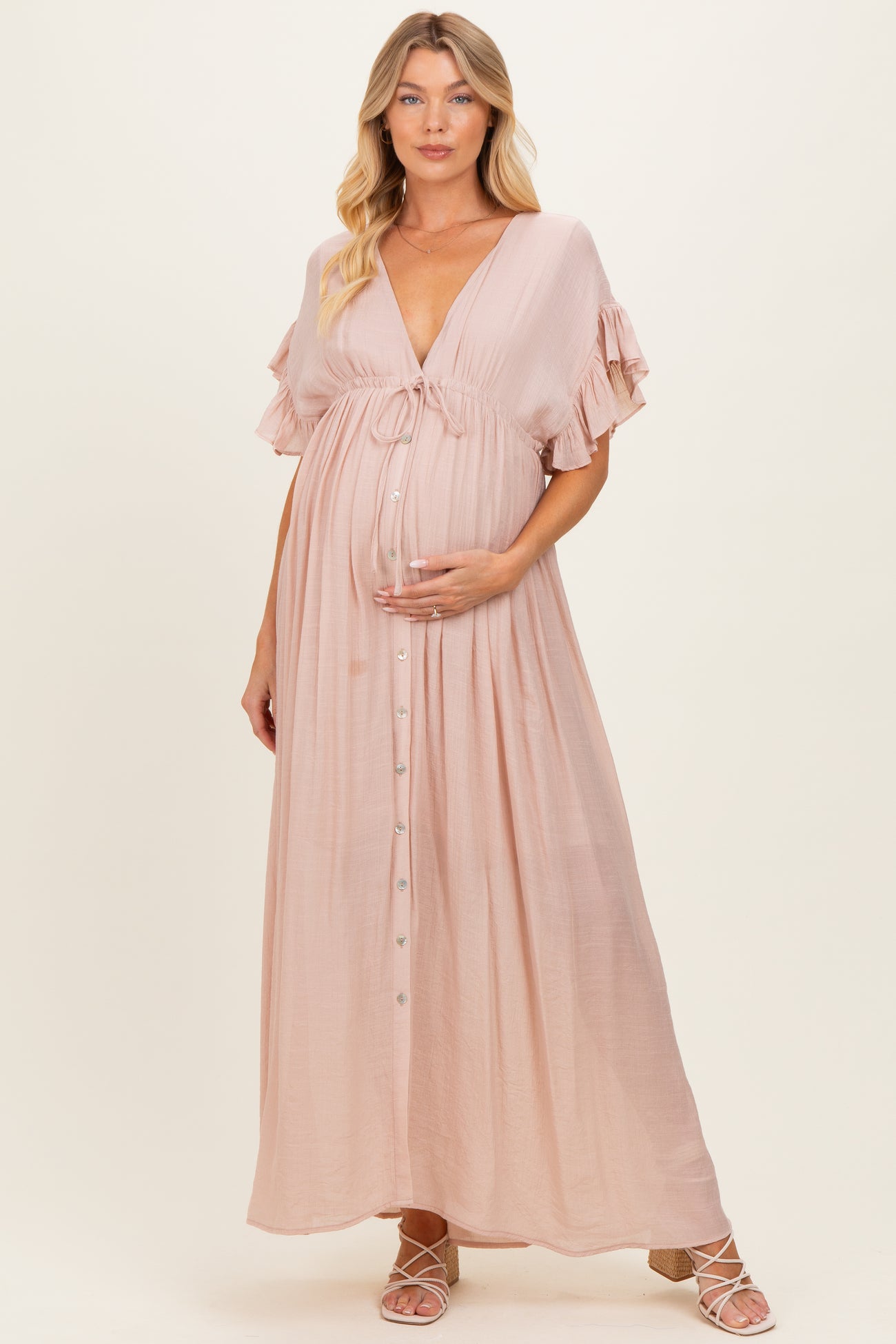 woman wearing a blush pink maternity maxi dress with ruffled sleeves and a button front, holding her baby bump