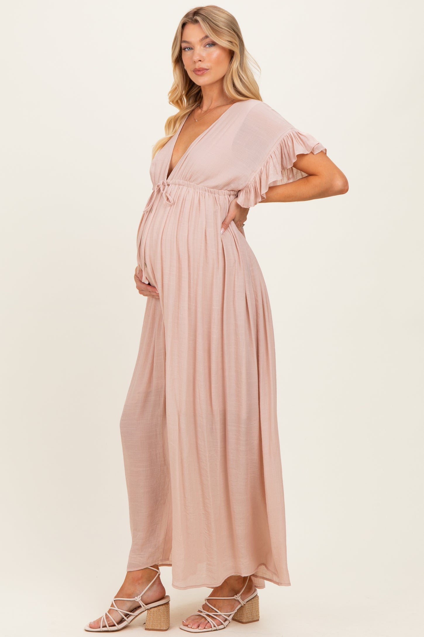 woman wearing a light pink maternity maxi dress with ruffled sleeves and a visible baby bump