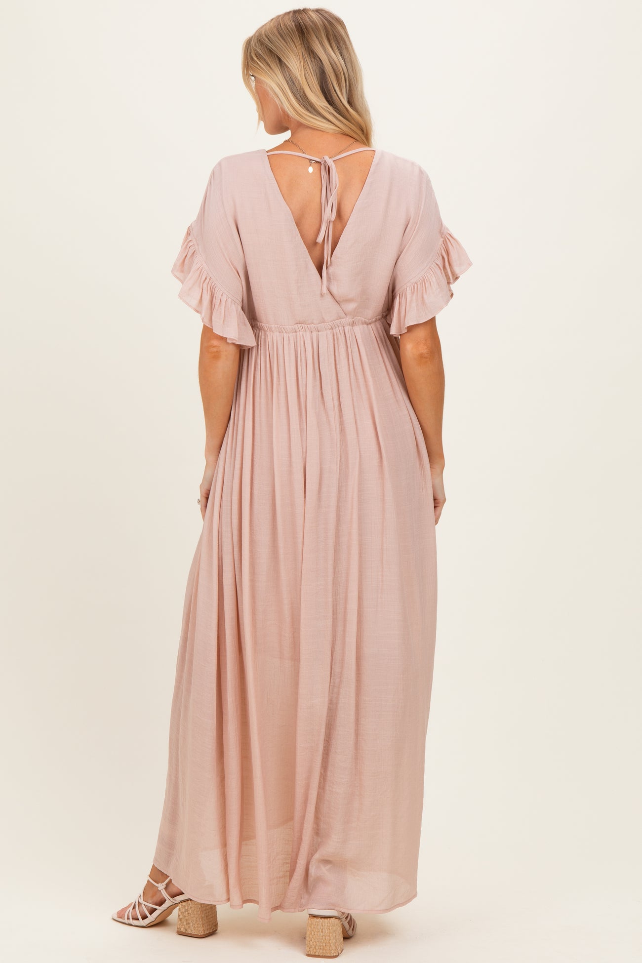 woman wearing a blush pink maternity maxi dress with flutter sleeves and a tie-back detail