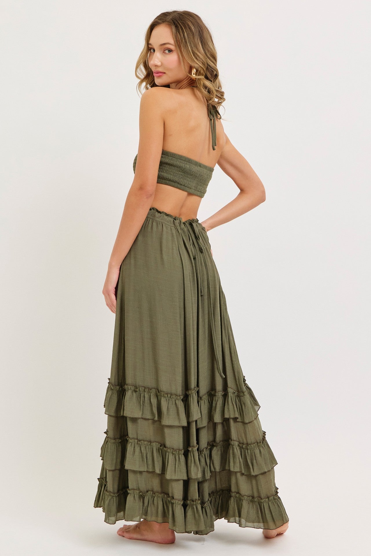 woman wearing a green two-piece set with a smocked crop top and a tiered maxi skirt, shown from the back