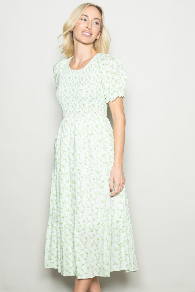 woman wearing a green floral midi dress with puff sleeves and a tiered skirt, standing and smiling