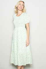 woman wearing a green floral midi dress with puff sleeves and a tiered skirt, standing and smiling