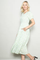 woman wearing a floral green midi dress with short puff sleeves and pockets, standing against a light background